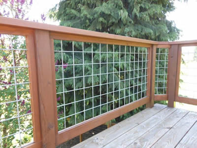 Welded wire cloth infill panel with square holes are installed on fences of wooden balcony outdoors.