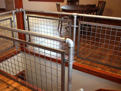 Woven crimped wire cloth infill panels with square holes are installed on fences of walkways indoors.